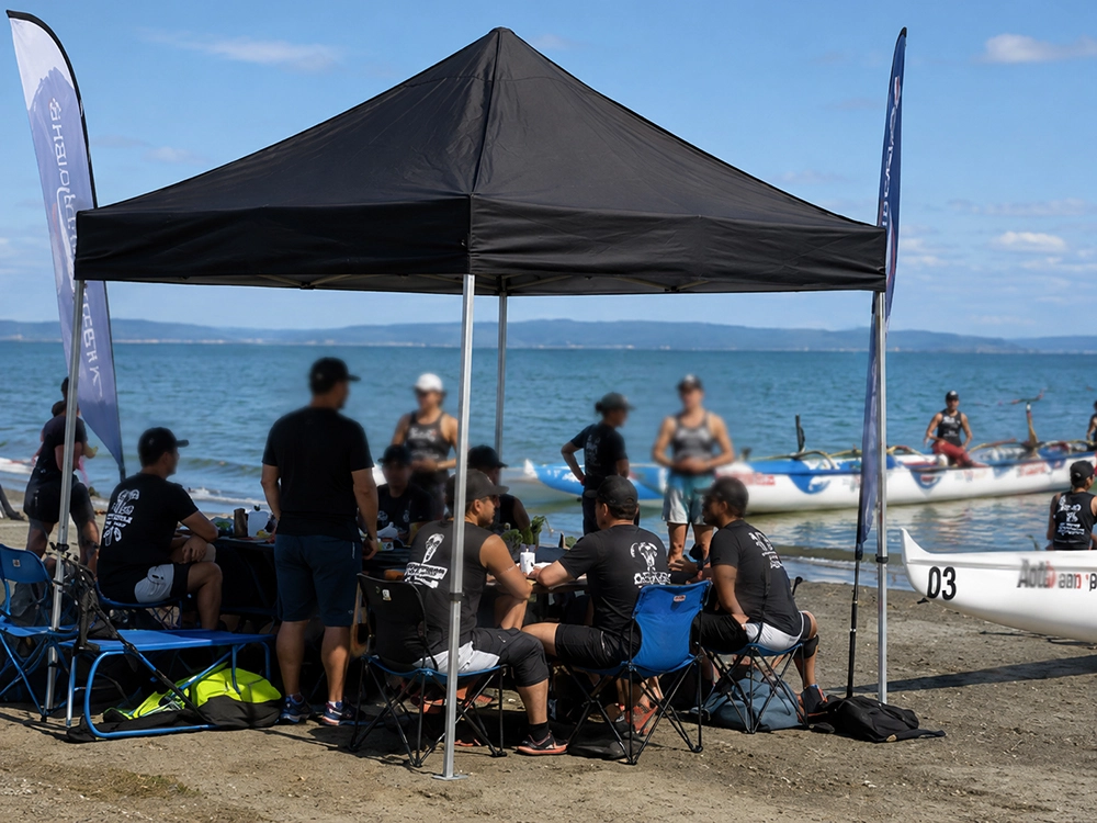 A black gazebo at a waka ama regatta on a New Zealand foreshore